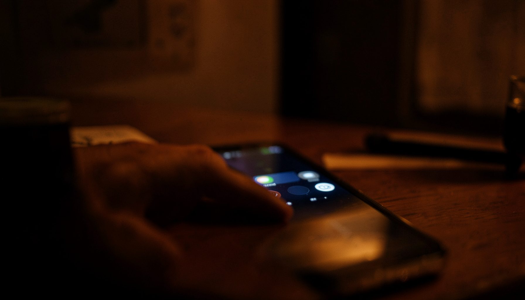 Moody interior scene with warm amber and deep shadow tones, a phone screen glowing softly in a dim room
