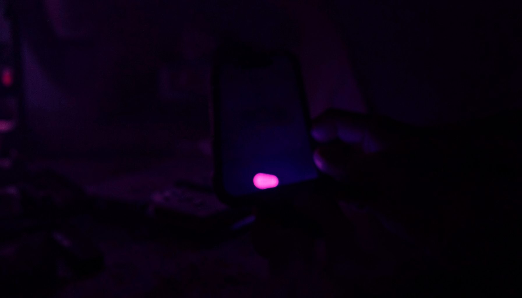 Dark atmospheric scene with deep purple and magenta lighting, a smartphone silhouette glowing against a moody backdrop, suggesting mobile gaming at night